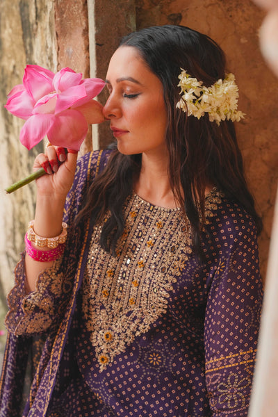 Woman in traditional kurta set attire holding a pink flower against a textured wall.Woman in traditional kurta set attire holding a pink flower against a textured wall.