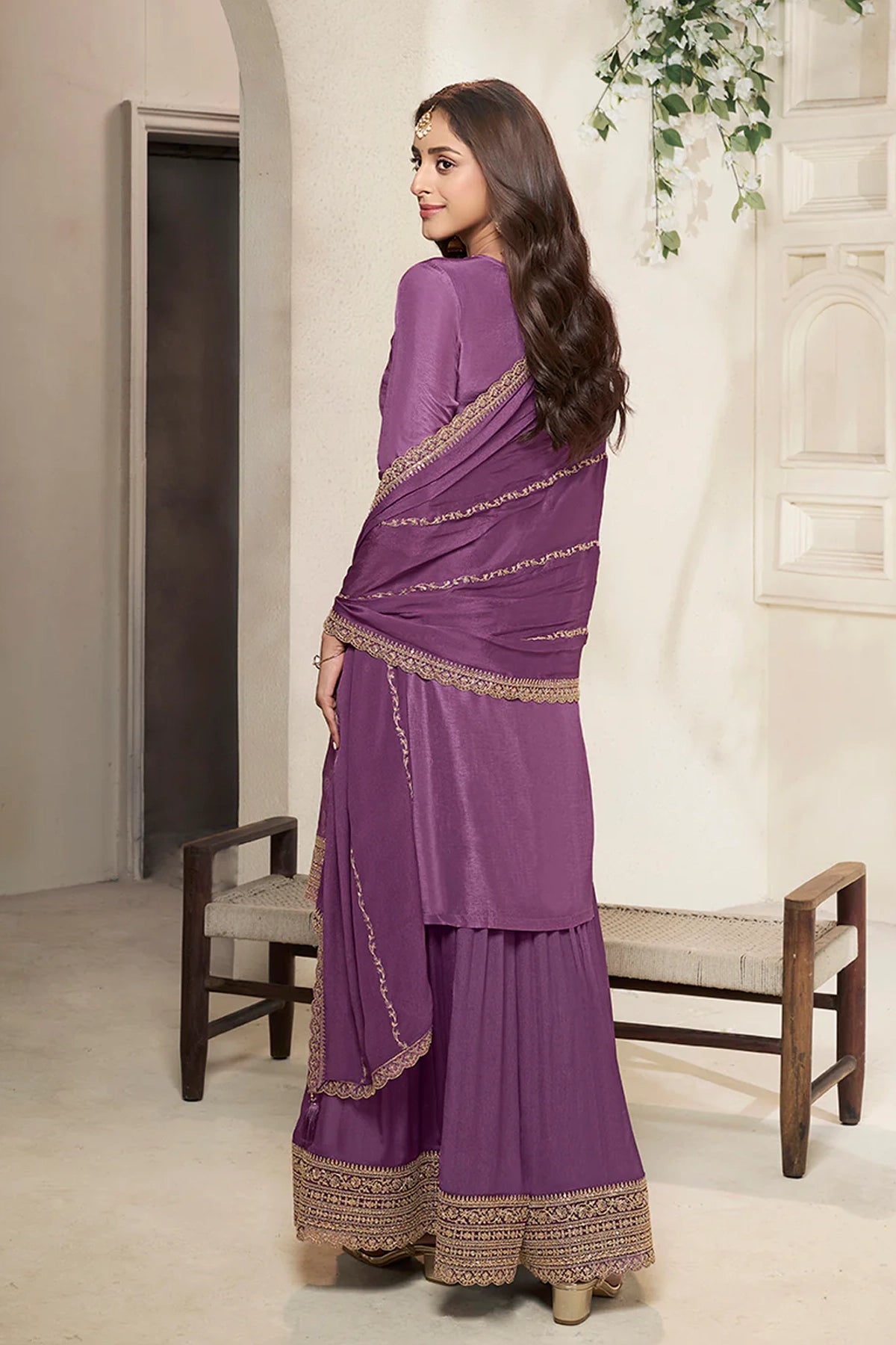 Woman wearing a purple sharara suit with gold border in an indoor setting