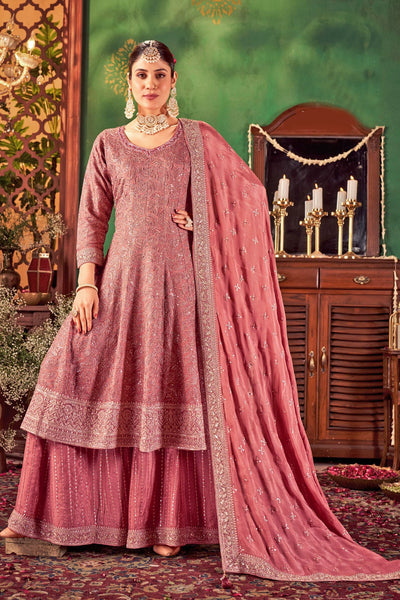 Woman in a traditional pink anarkali outfit with a matching dupatta against a decorative background.