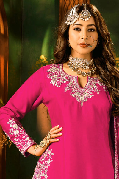 Woman wearing a pink traditional sharara outfit with intricate embroidery and jewelry against a blurred background.Woman wearing a pink traditional sharara outfit with intricate embroidery and jewelry against a blurred background.