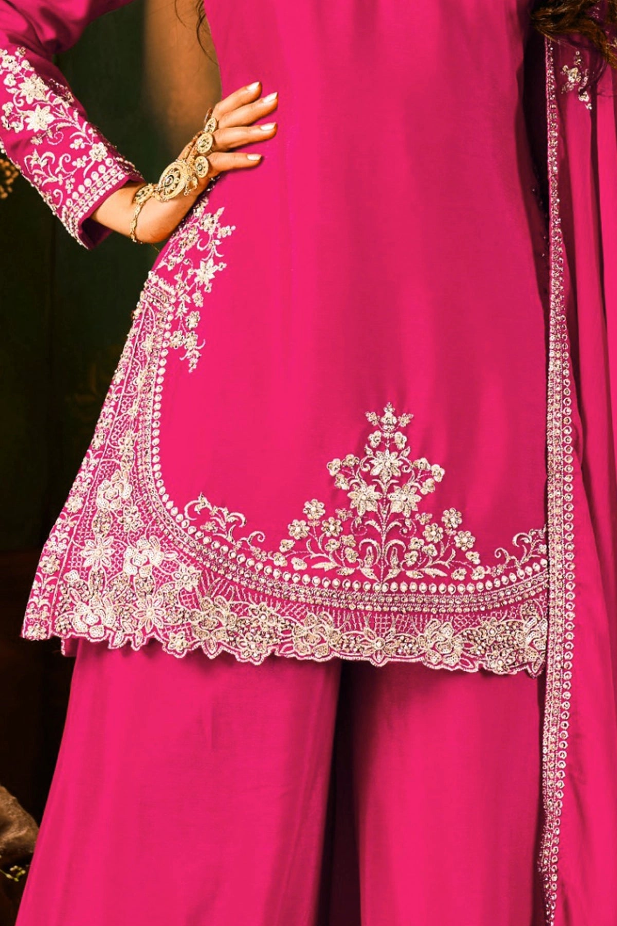 Pink traditional sharara outfit with intricate white embroidery on a dark background