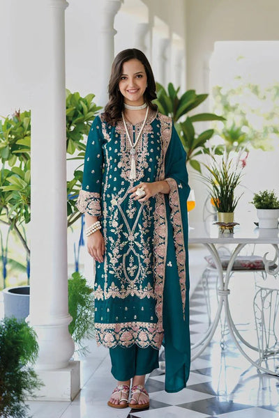 Woman in a teal and pink traditional outfit standing in an elegant indoor setting with plants.