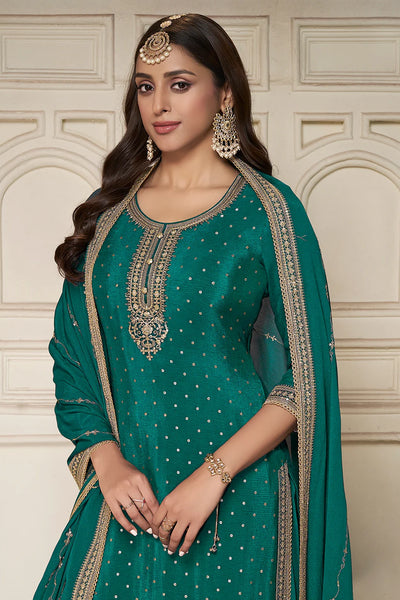 Woman wearing a teal green sharara suit  traditional outfit with intricate embroidery against a white wall.Woman wearing a teal green sharara suit  traditional outfit with intricate embroidery against a white wall.