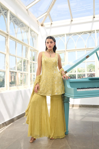 Woman in a Light Yellow Georgette Sharara Suit outfit standing next to a blue piano in a sunlit room with large windows.Woman in a Light Yellow Georgette Sharara Suit outfit standing next to a blue piano in a sunlit room with large windows.