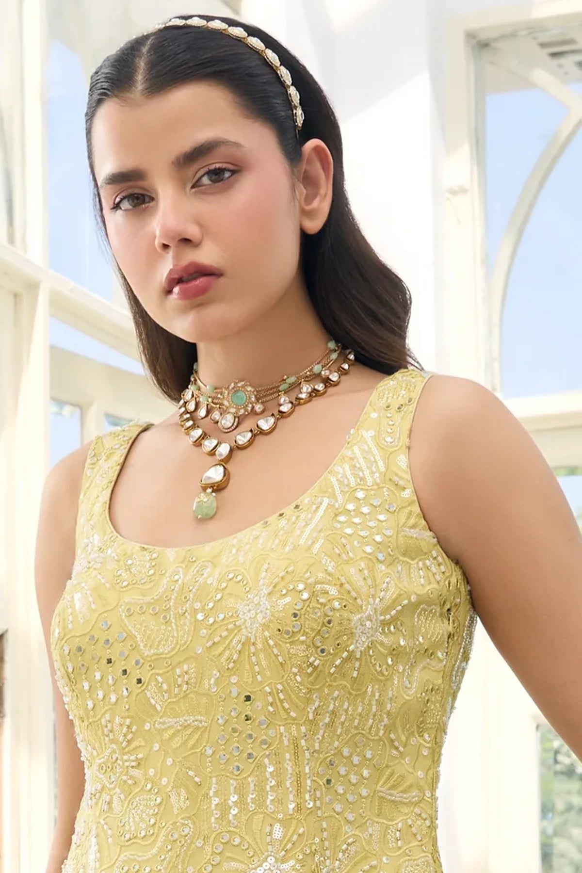 Woman wearing a Light Yellow Georgette Sharara Suit with intricate patterns and jewelry, standing in a bright indoor setting.