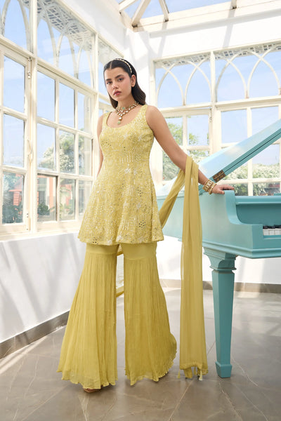 Woman in a  Light Yellow Georgette Sharara Suit traditional outfit standing in a room with large windows and a blue piano.